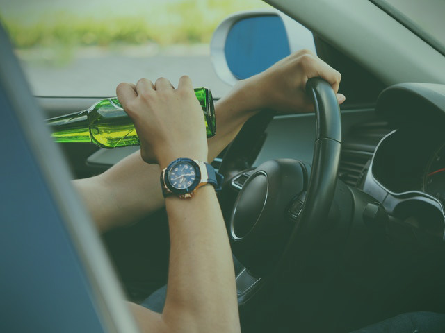 driver behind the wheel taking a sip from a beer bottle