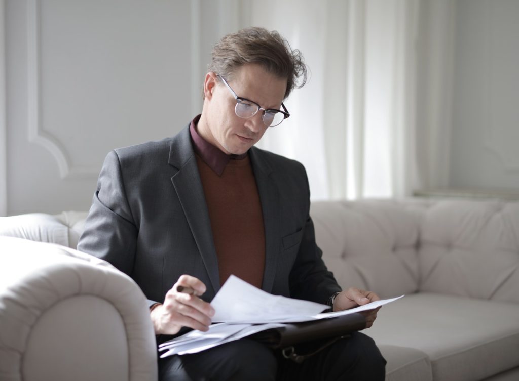 man sitting on a white couch reading through paperwork